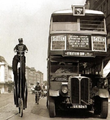 Streatham sudul Londrei 1932. Șoferul autobuzului aruncând o privire la un artist de circ pe o bicicletă de lângă el care își promovează sosirea spectacolului la Clapham Common